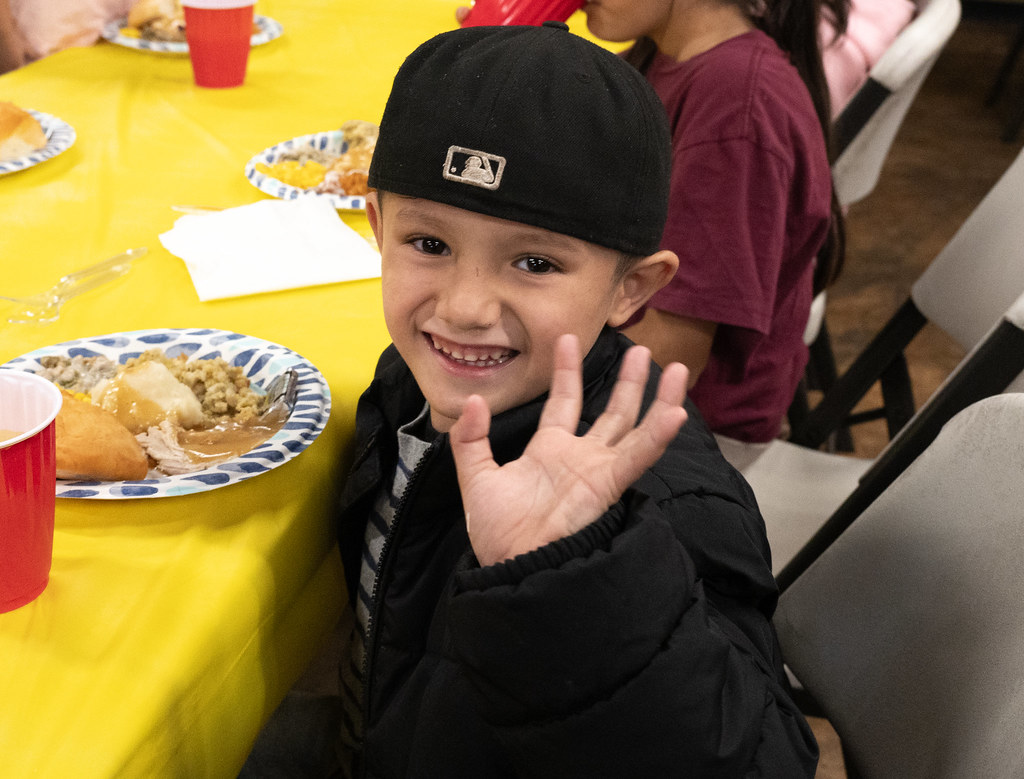 Boy smiling and waving beside a plate of Thanksgiving food